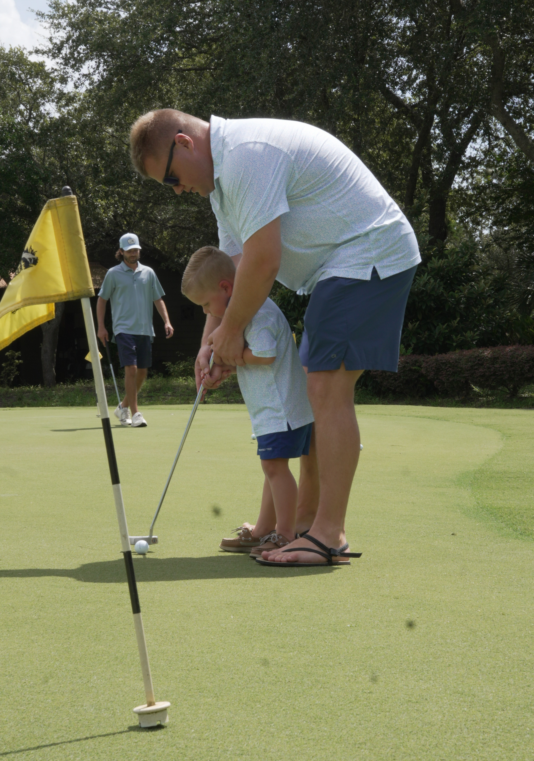 Father helping young child learn golf during Family Golf Week